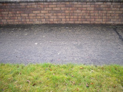 Photo of photo of a path between a grass verge and a brick wall